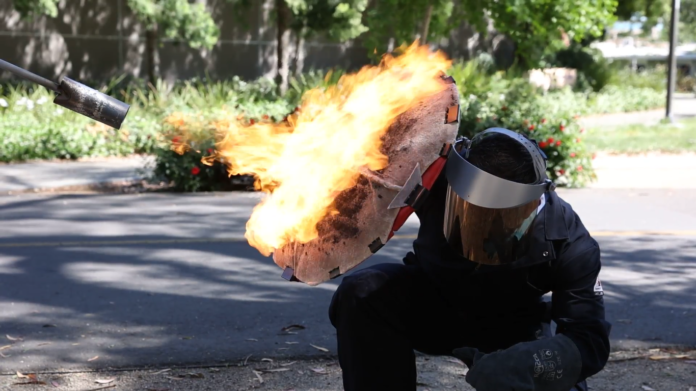 A person shielding themselves from flames and wearing a helmet dressed as a superhero
