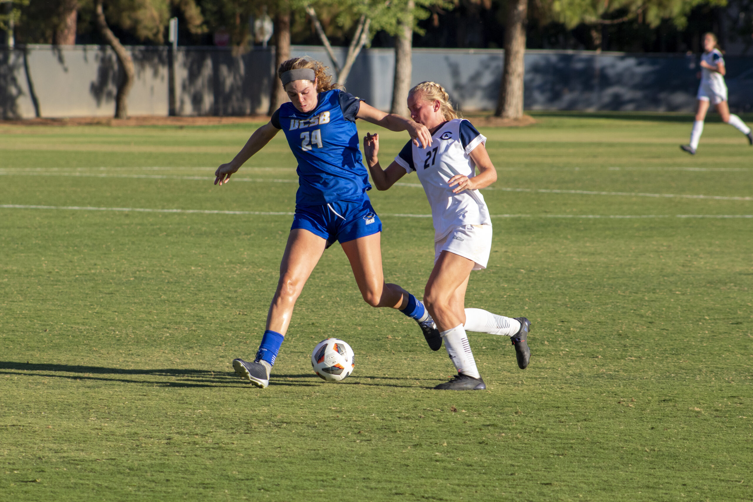 Two women playing soccer, Aggie's try to steal the ball.